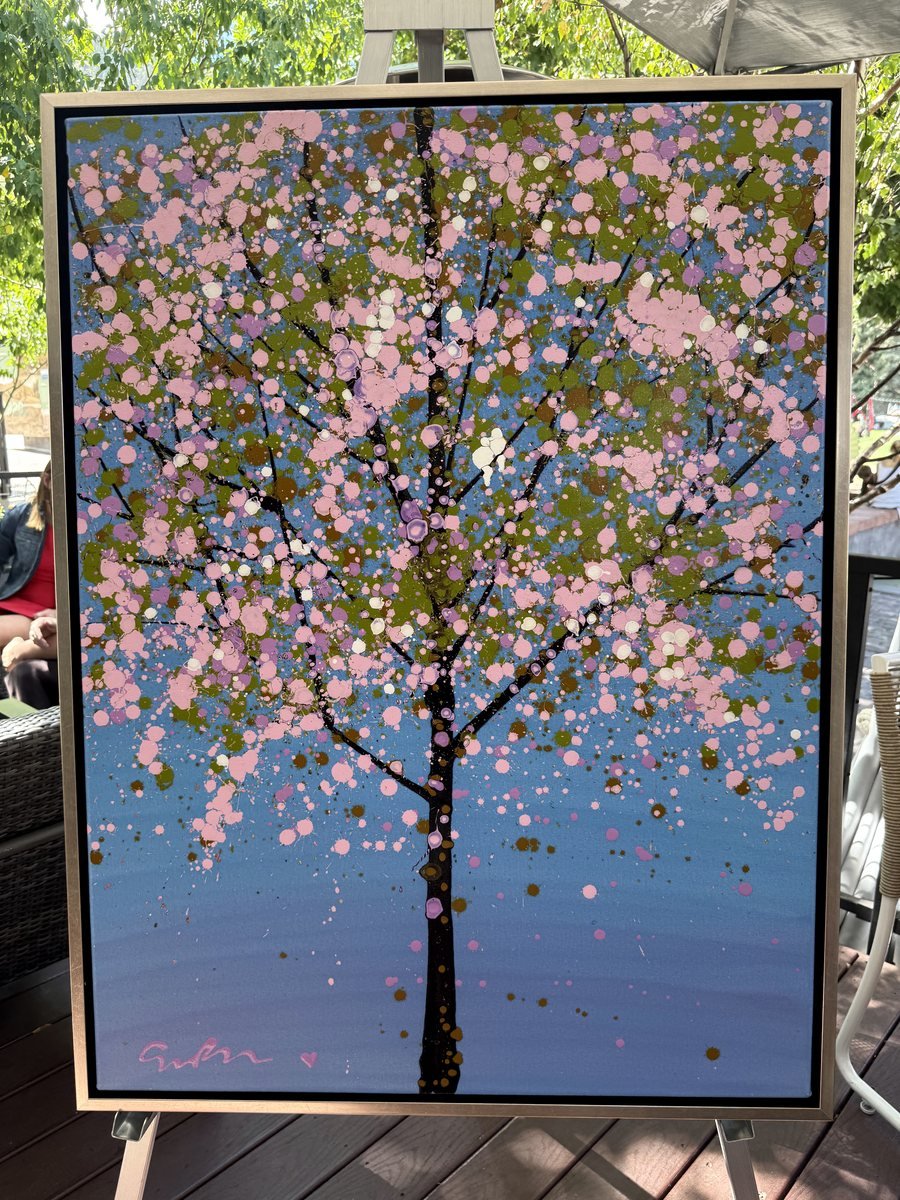 A Simon Bull painting of a blossoming tree in pink, olive and blue, on an easel on the Bosq patio