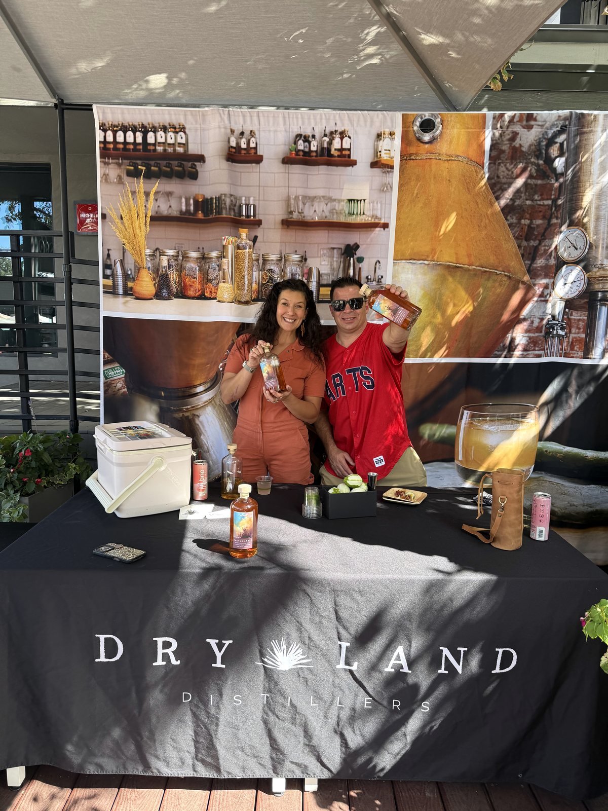 Kelly Dressman and Scott McDowell holding bottles of Cactus Añejo behind the Dry Land Distillers table on the Bosq patio
