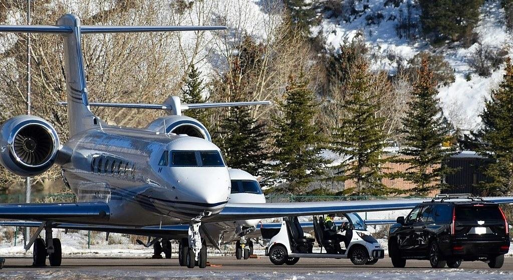 A private jet on the ramp at Aspen with vehicles waiting alongside in winter