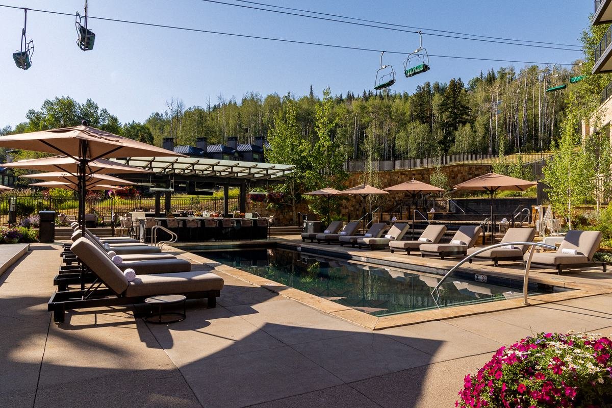 The Lift Line pool deck at Viceroy Snowmass, with a chairlift running overhead and aspen and evergreen slopes behind