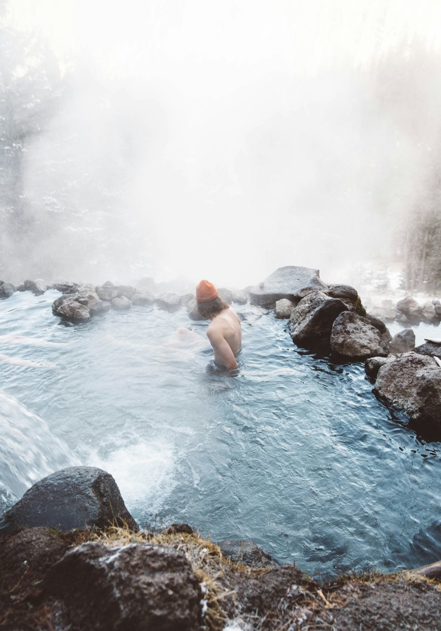 A person soaking in a steaming natural hot spring surrounded by snow and rock