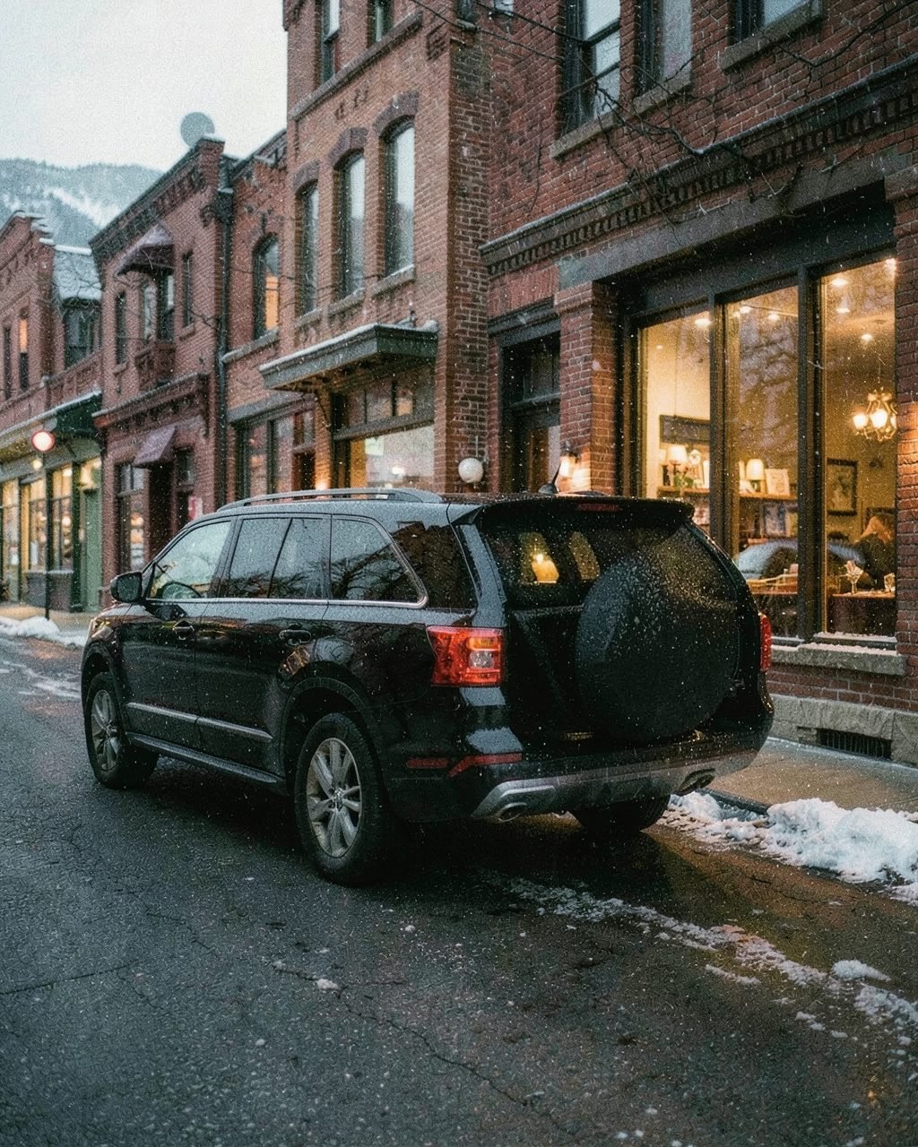 A black SUV waiting at the curb on a snowy brick street in Aspen