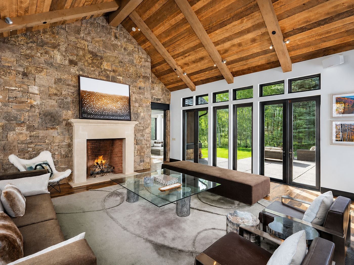 The great room, with stone fireplace, vaulted reclaimed timber ceiling and a wall of glass opening to the terrace
