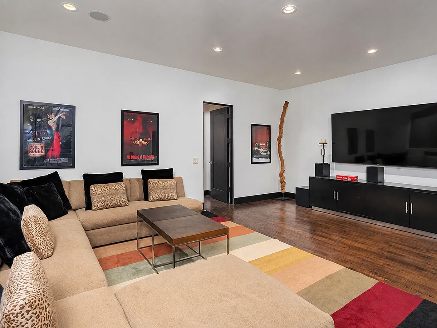 The lower level living area, with a large sectional, framed film posters and a wall-mounted television