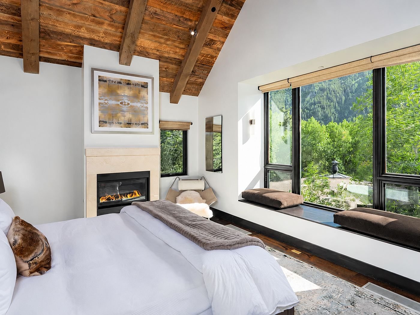 The primary bedroom, with a fireplace, timber ceiling and a window seat looking into trees