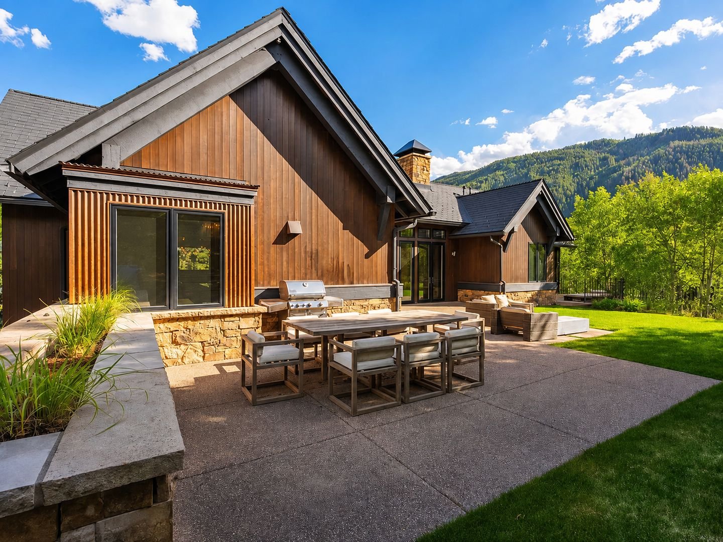 The terrace outside the main level, with dining table, grill and lawn, mountainside beyond