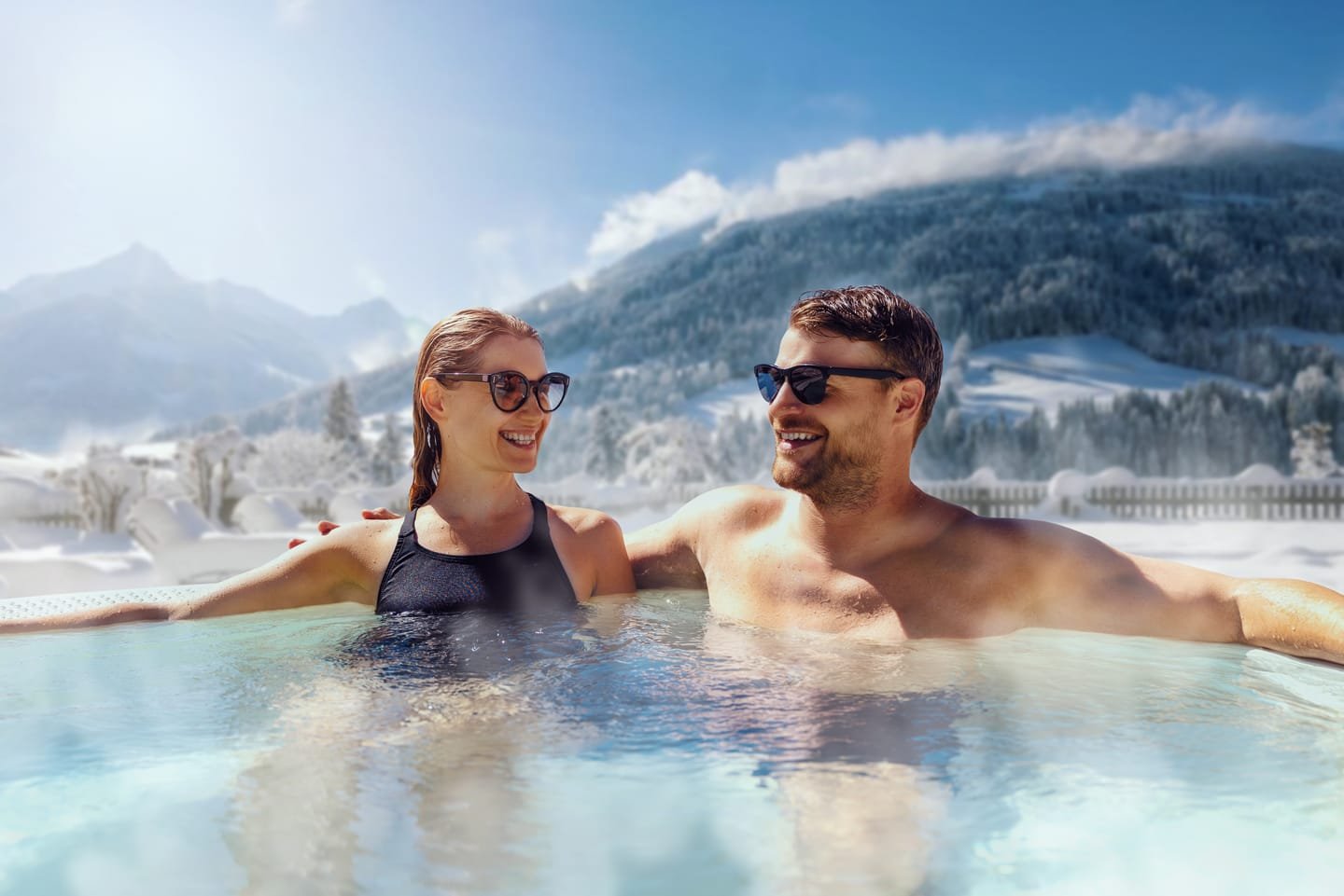 A couple in an outdoor hot tub with snowy mountains behind