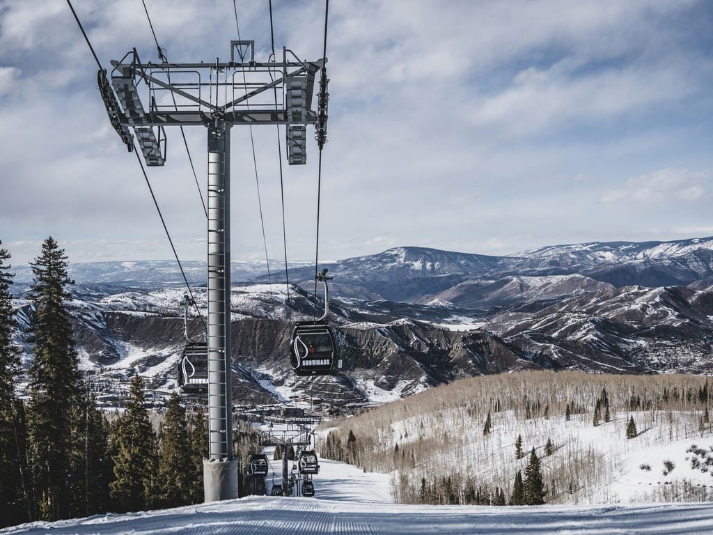 A gondola line above groomed snow in Aspen, the valley and peaks beyond