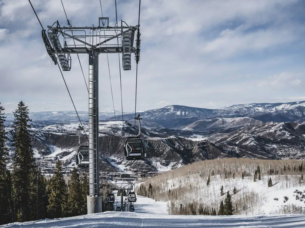 Una línea de góndola sobre nieve pisada en Aspen, con el valle y las cumbres al fondo